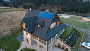 Una casa grande de varios pisos con techo a dos aguas, paneles solares y base de piedra.