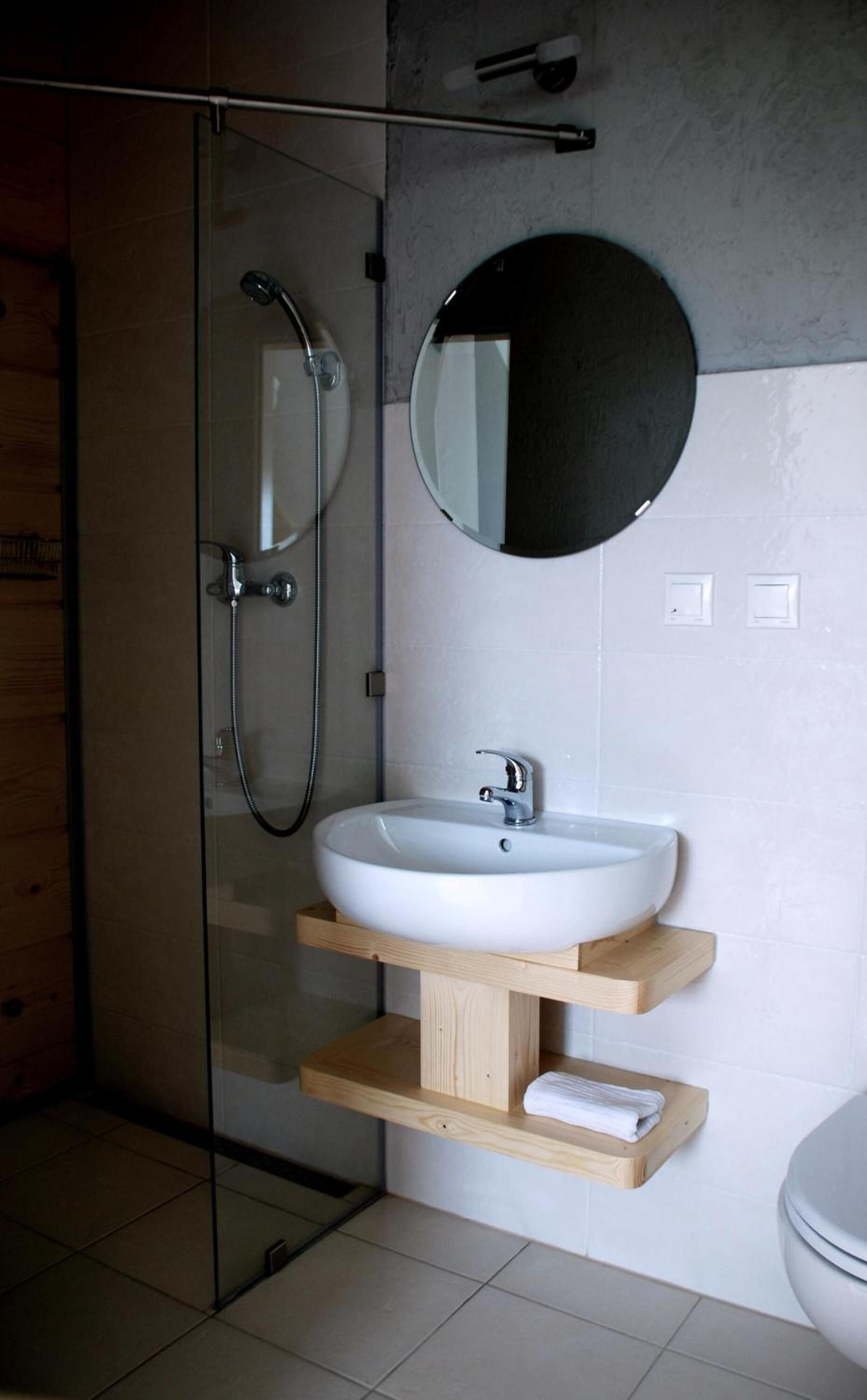 Une salle de bain moderne avec une douche à l’italienne en verre, un lavabo blanc et un miroir rond.