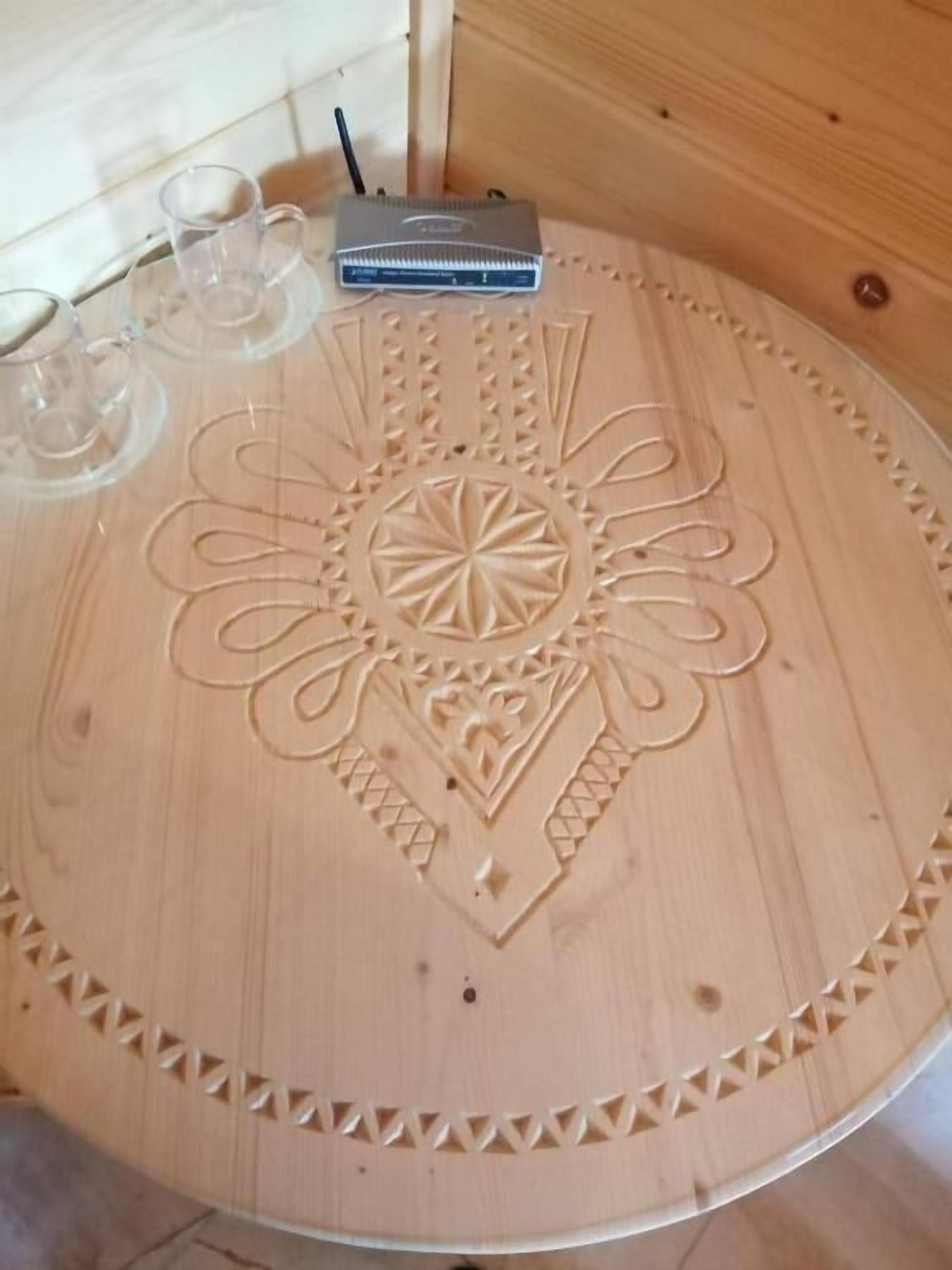 A round wooden table with a carved floral pattern, a laptop, and two glasses on it.