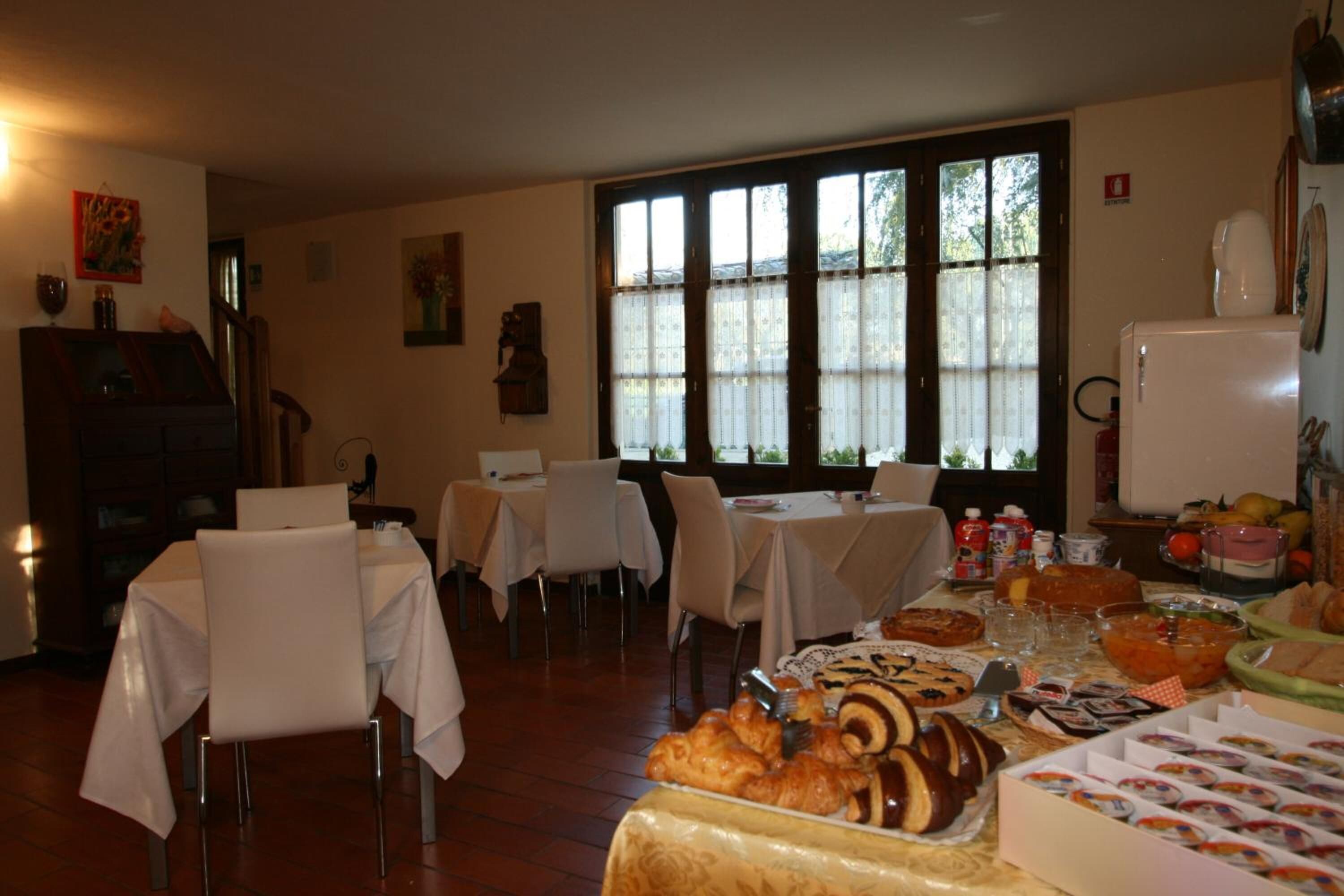 A dining area with tables set for a meal, a buffet with various food items, and a refrigerator in the background.
