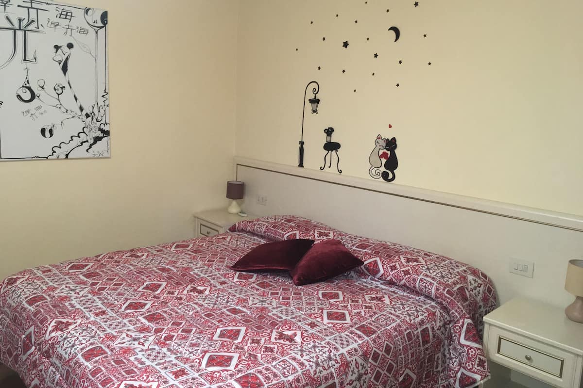 Un dormitorio con cama, mesita de noche, lámpara y un adorno en la pared.