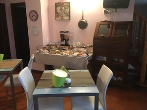 A dining area with a table set for two, a green cup, and various food items on a buffet table. - La Stregatta B&B (Fucecchio)