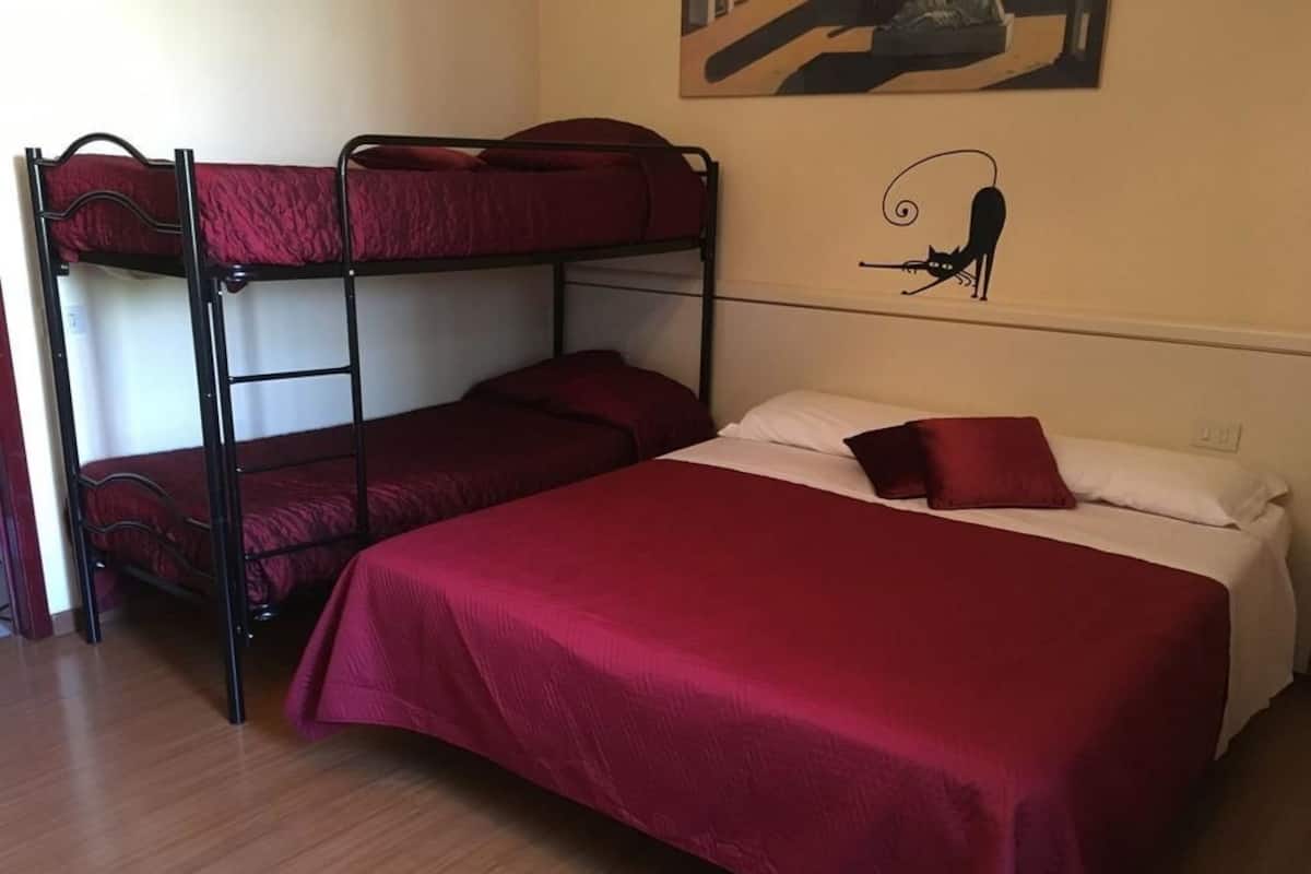 Habitación con literas, colcha roja y un cuadro de un gato en la pared.
