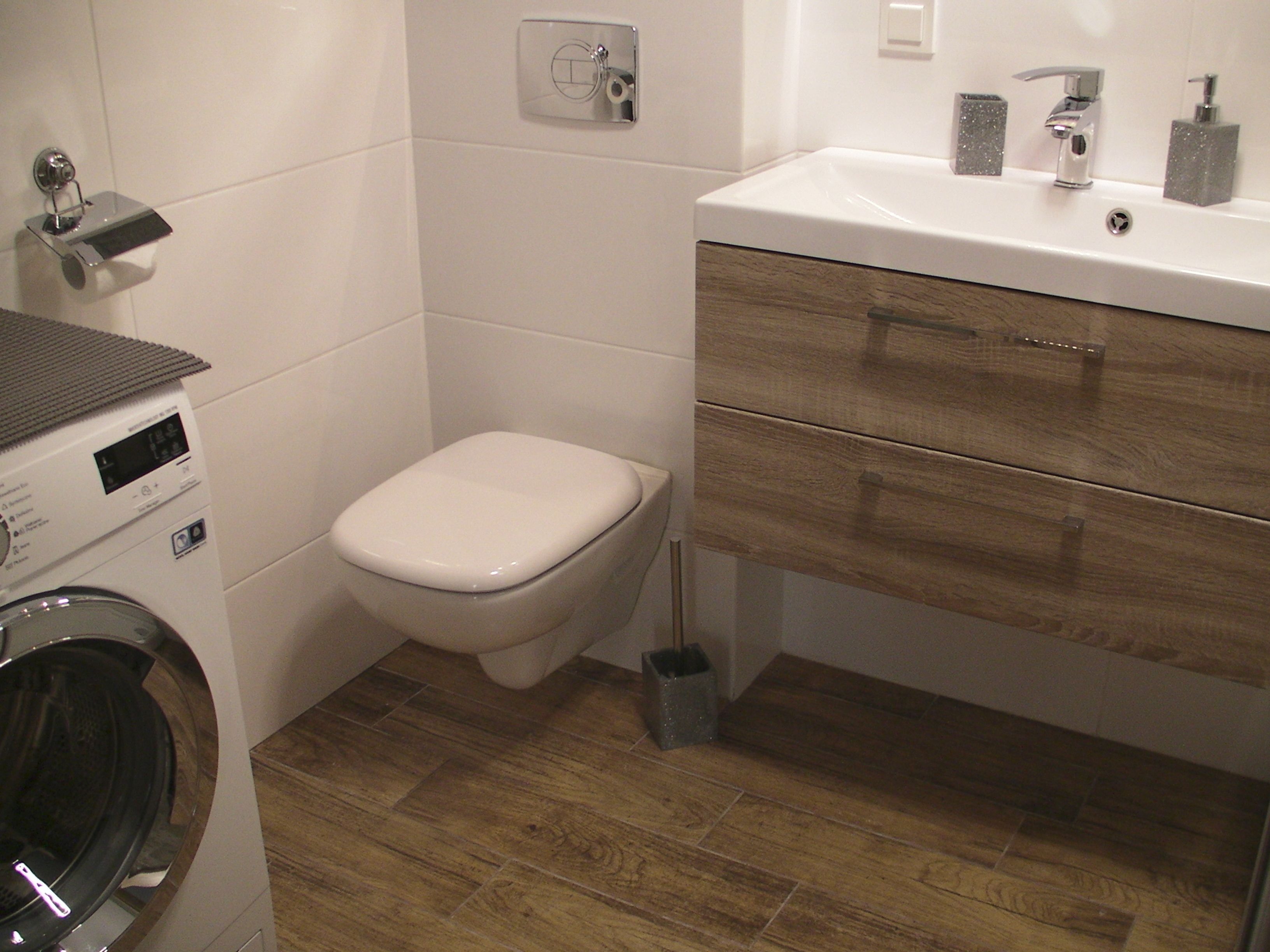A modern bathroom with a toilet, washing machine, and wooden vanity.