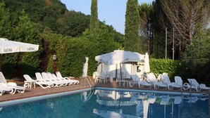 A swimming pool with lounge chairs and umbrellas, surrounded by trees and a hill.