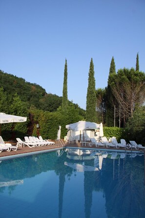 A swimming pool with lounge chairs and umbrellas, surrounded by trees and a hill. - Ristorante Albergo Felcaro (Cormons)