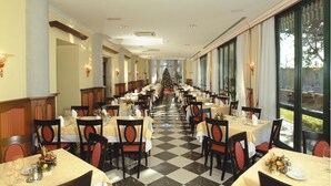 Un comedor largo con mesas dispuestas para una comida, un árbol de Navidad en el centro y ventanas amplias a un lado.