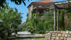 Um edifício de pedra com telhado de telhas, cercado por vegetação exuberante e um caminho de cascalho.