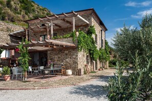 Ein Steingebäude mit einer Pergola, Sitzgelegenheiten im Freien und einem Kieshof.