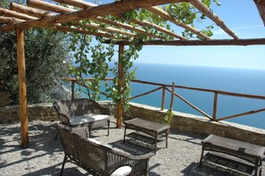 A wooden pergola with wicker furniture overlooking a coastal view.