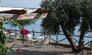 Ein Außenbereich mit Korbstühlen und Tischen, einer Holzpergola und Blick aufs Meer.