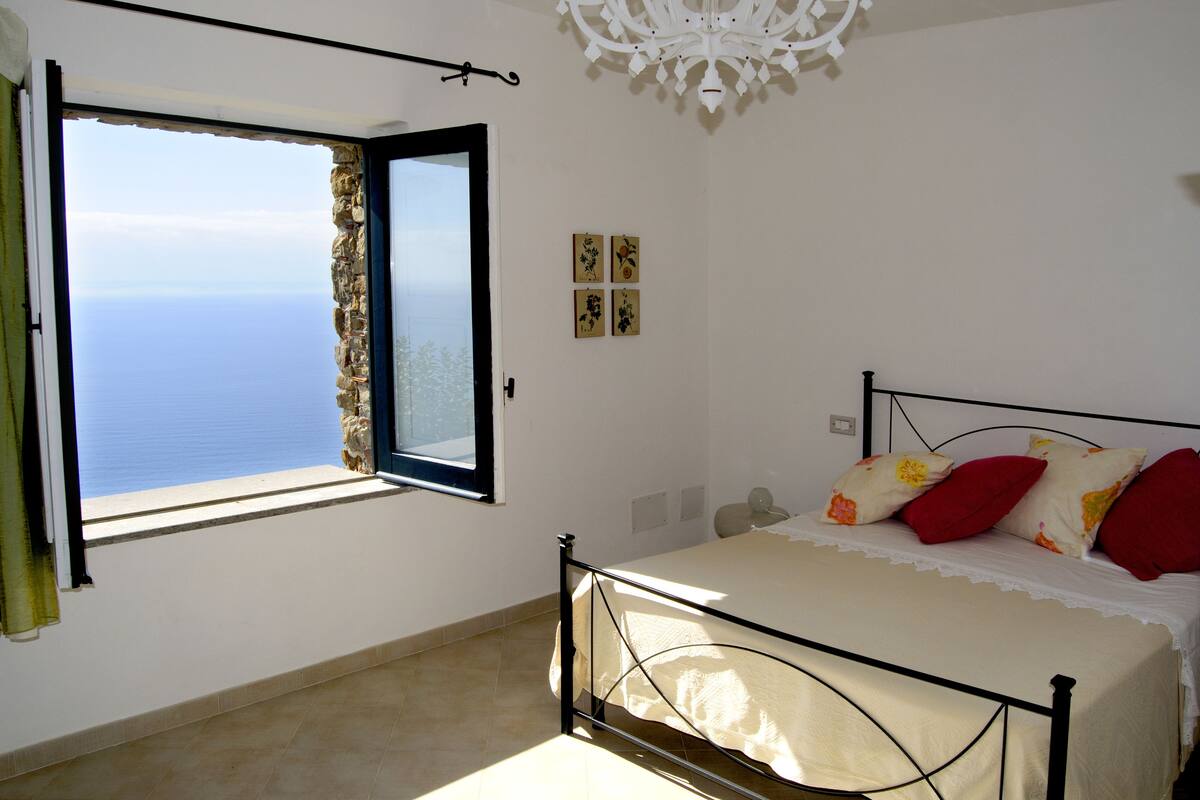 Un dormitorio con cama, ventana con vista al mar, candelabro y decoración en la pared.