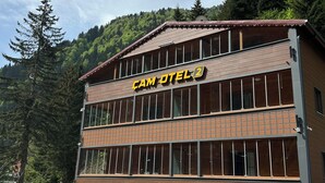 A two-story building with a sign reading "CAM OTEL" and a view of a forested hillside in the background. - Çam Otel 2 (Çaykara)