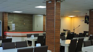 Un restaurante con mesas blancas y sillas negras, un revestimiento de pared de madera y una barra con una luz roja.