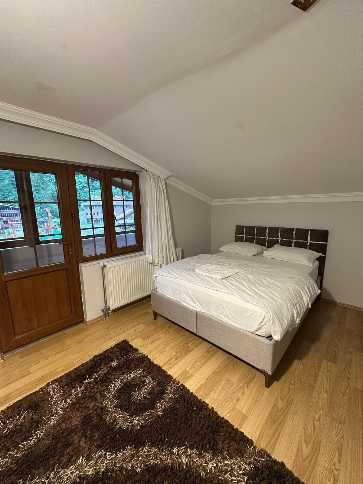 Een slaapkamer met een bed, een raam met gordijnen, een radiator en een houten vloer.