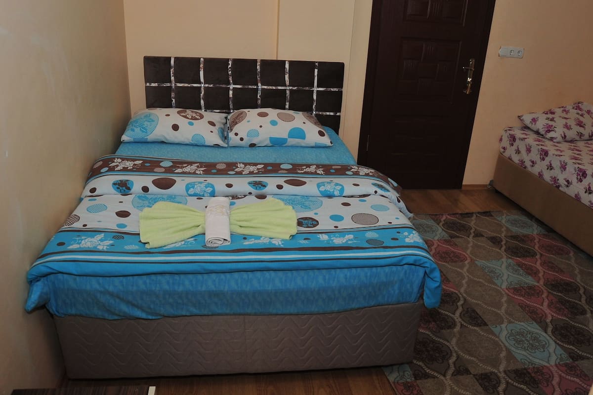 A bed with a patterned bedspread, pillows, and a green towel.