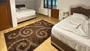A bedroom with two beds, a wooden floor, a large rug, and a window with curtains. - Çam Otel 2 (Çaykara)