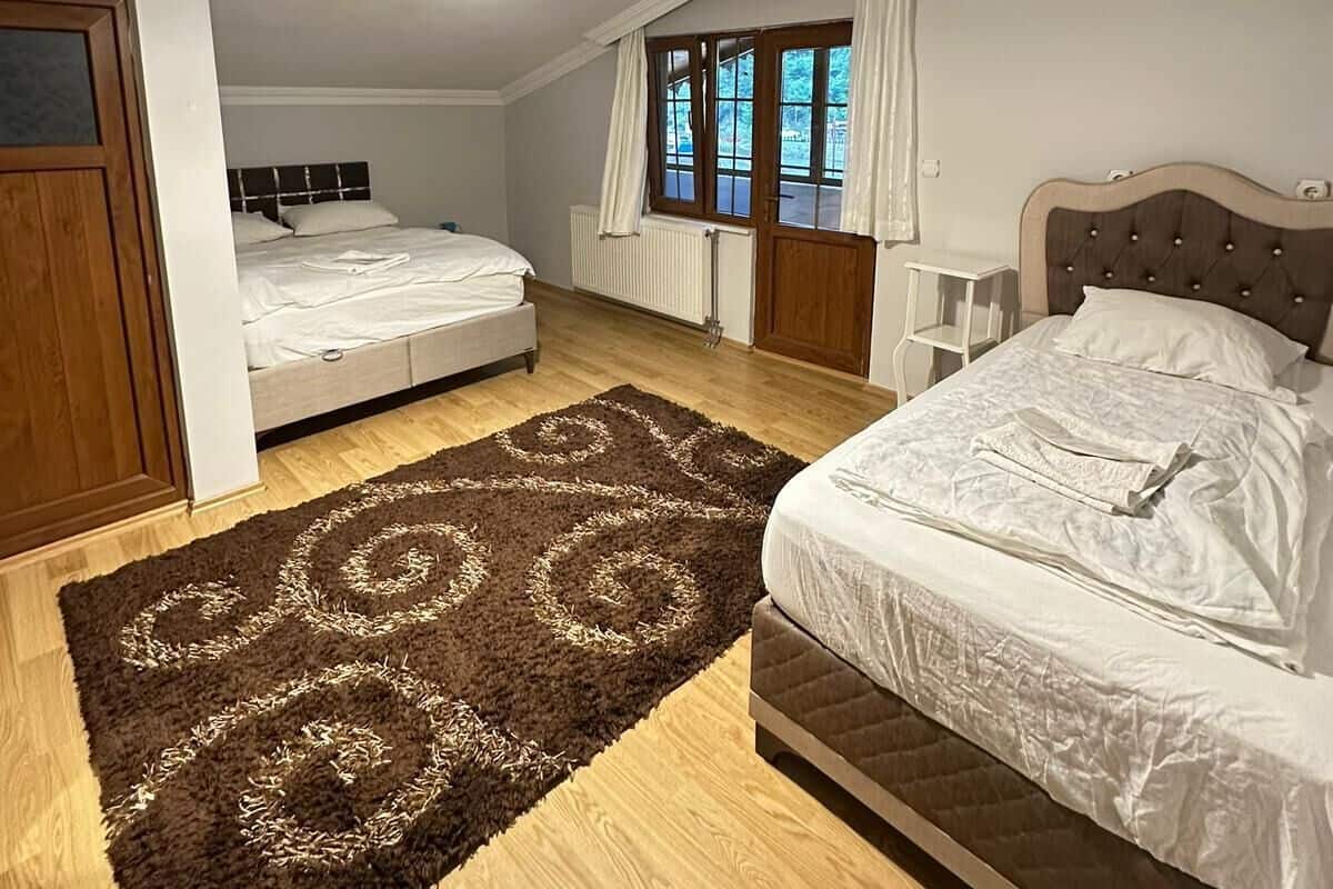 A bedroom with two beds, a wooden floor, a large rug, and a window with curtains.