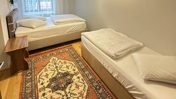 Un dormitorio con dos camas, un tapete estampado, una lámpara en el techo y una ventana con cortinas.