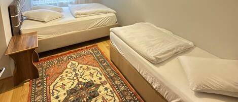A bedroom with two beds, a patterned rug, a ceiling light, and a window with curtains.