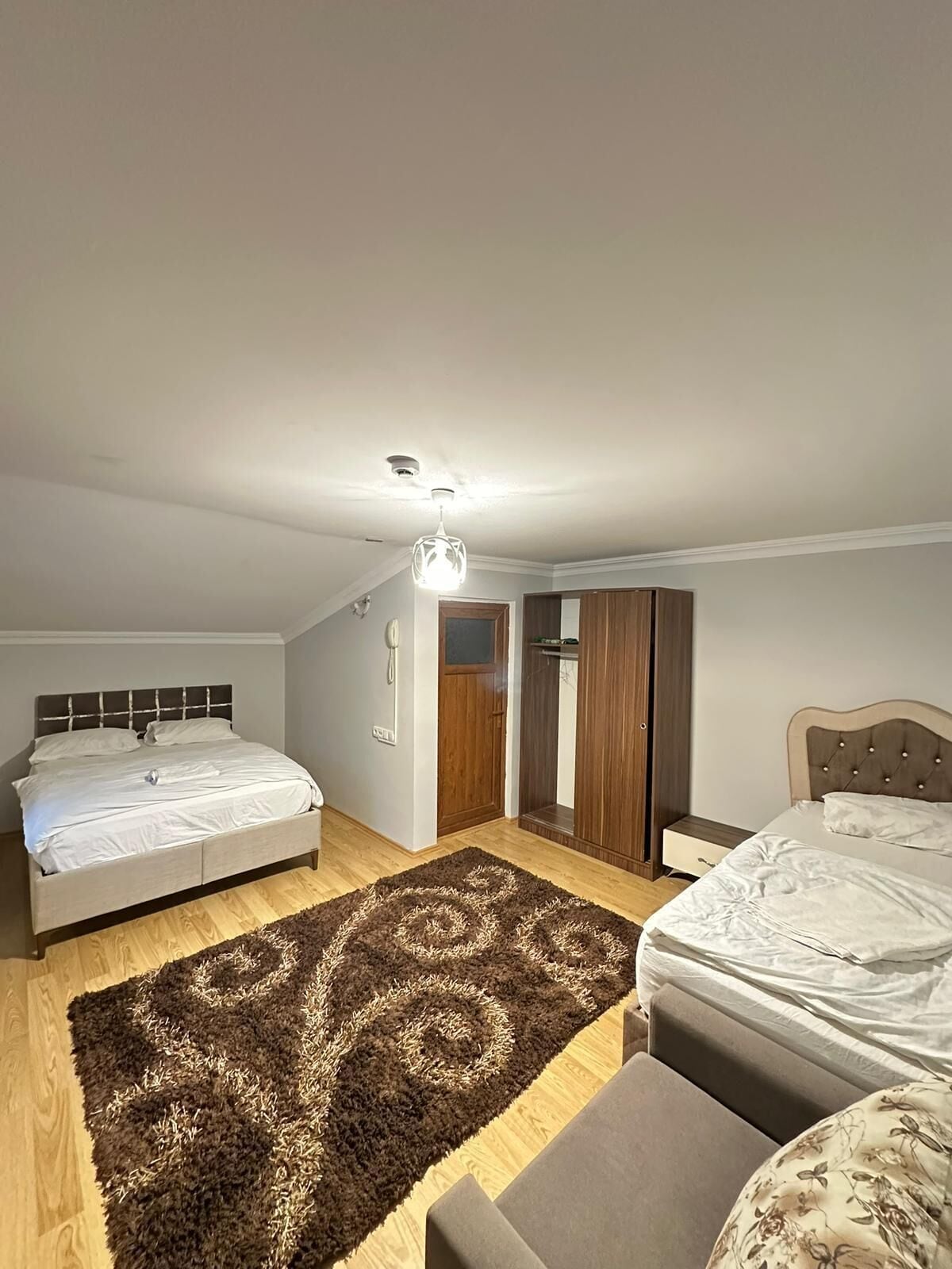 A bedroom with two beds, a ceiling fan, a wooden wardrobe, and a patterned rug.