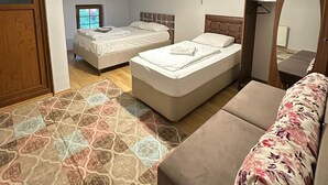 A bedroom with two beds, a sofa, a patterned rug, and a ceiling fan. - Çam Otel 2 (Çaykara)