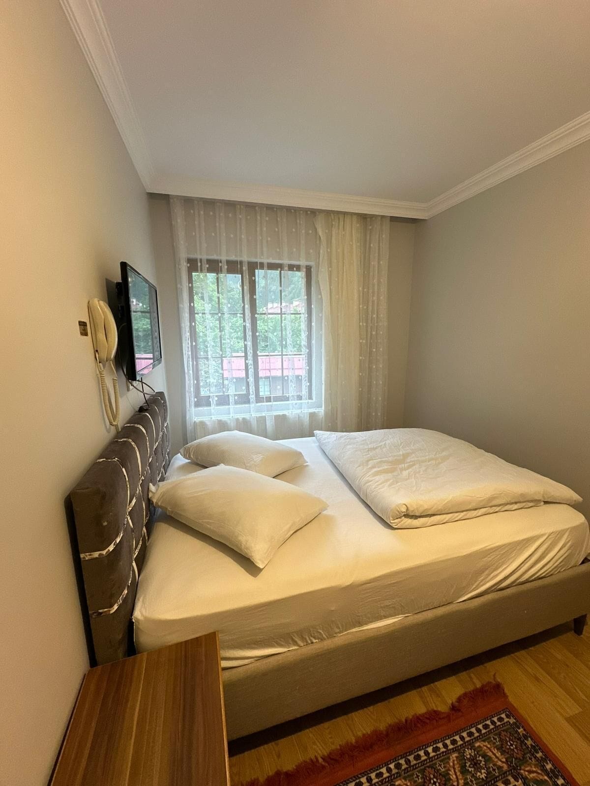 Quarto com cama, televisão, telefone e janela com cortinas.