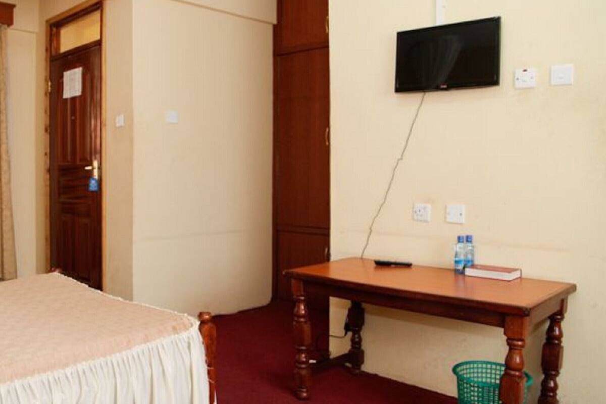 A room with a bed, a desk, a television, and a window with curtains.