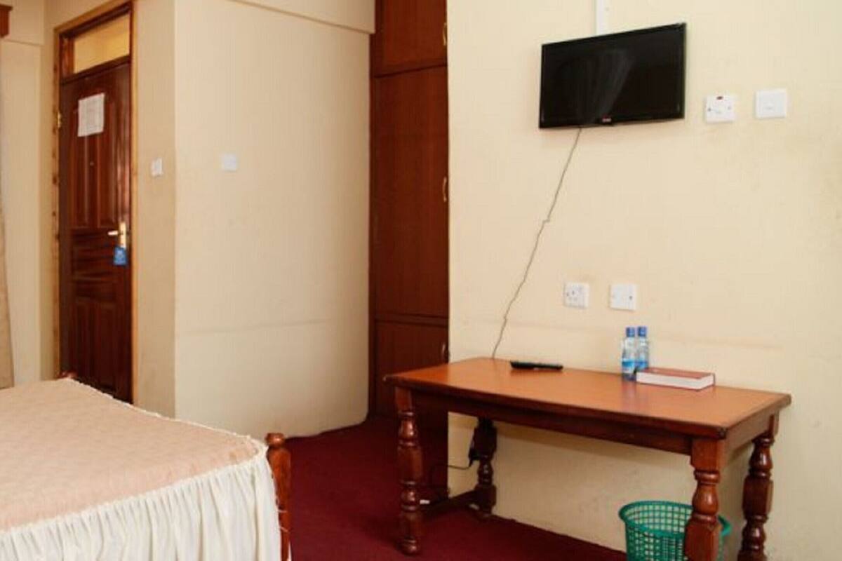 A hotel room with a bed, a wooden desk, a television mounted on the wall, and a window with curtains.