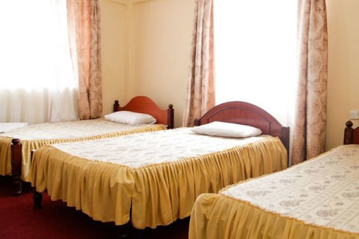 A hotel room with three single beds, each with a wooden headboard and a yellow bed skirt.