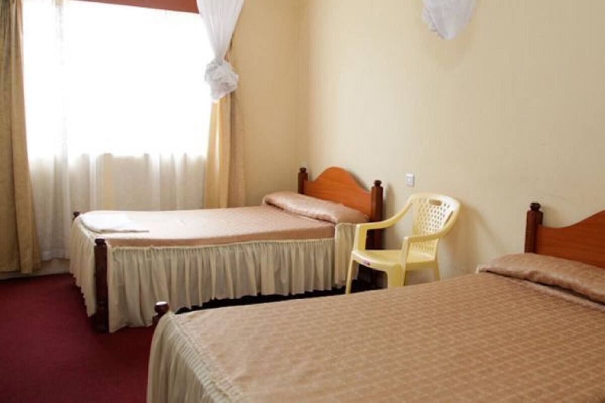 A room with two beds, a chair, and a window with curtains.