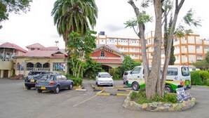 A multi-story building with a red roof and a sign that reads "Cool Rivers." There are cars parked in front, and a van with a "Keep Left" sign is visible. - Cool Rivers Hotel (Nakuru)