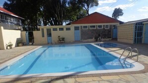 A swimming pool with a stone deck, surrounded by buildings with red roofs and blue doors. - Cool Rivers Hotel (Nakuru)
