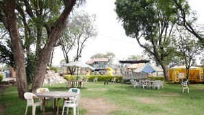 An outdoor area with picnic tables and chairs, a playground with a slide, and a yellow playhouse. - Cool Rivers Hotel (Nakuru)