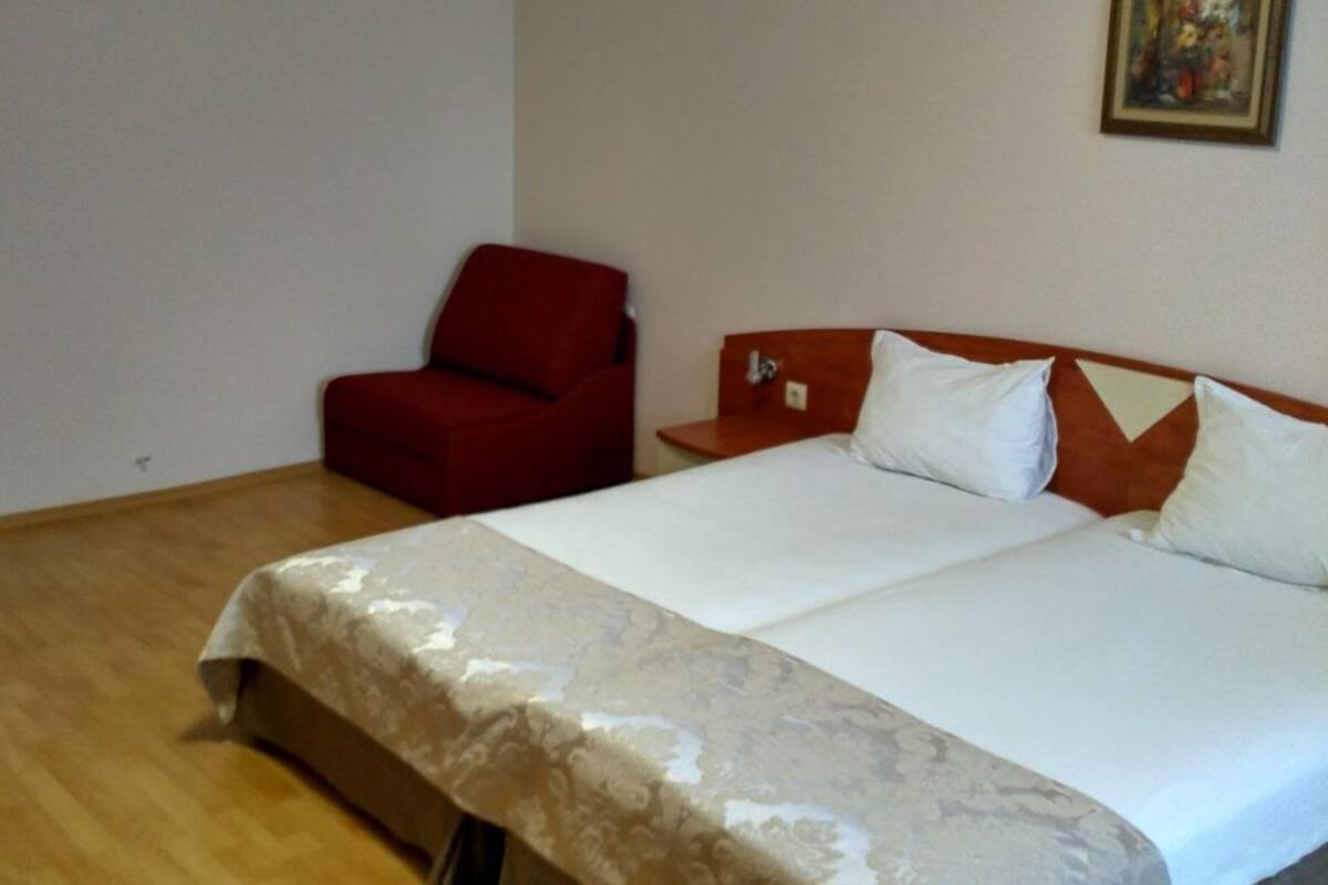 Habitación de hotel con una cama grande, un sillón rojo, una mesita y un cuadro en la pared.
