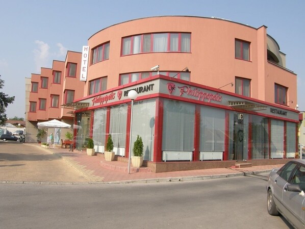 Een hotel met een gebogen gevel, een restaurant op de begane grond en een bord dat het hotel aanduidt.
