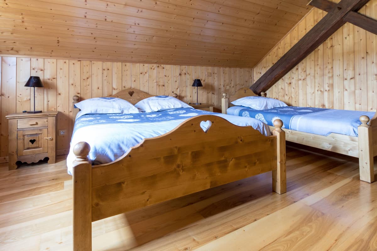 Une pièce aux murs lambrés, avec deux lits en bois, chacun doté d’une tête de lit en forme de cœur, et une petite armoire en bois ornée d’une découpe en forme de cœur.