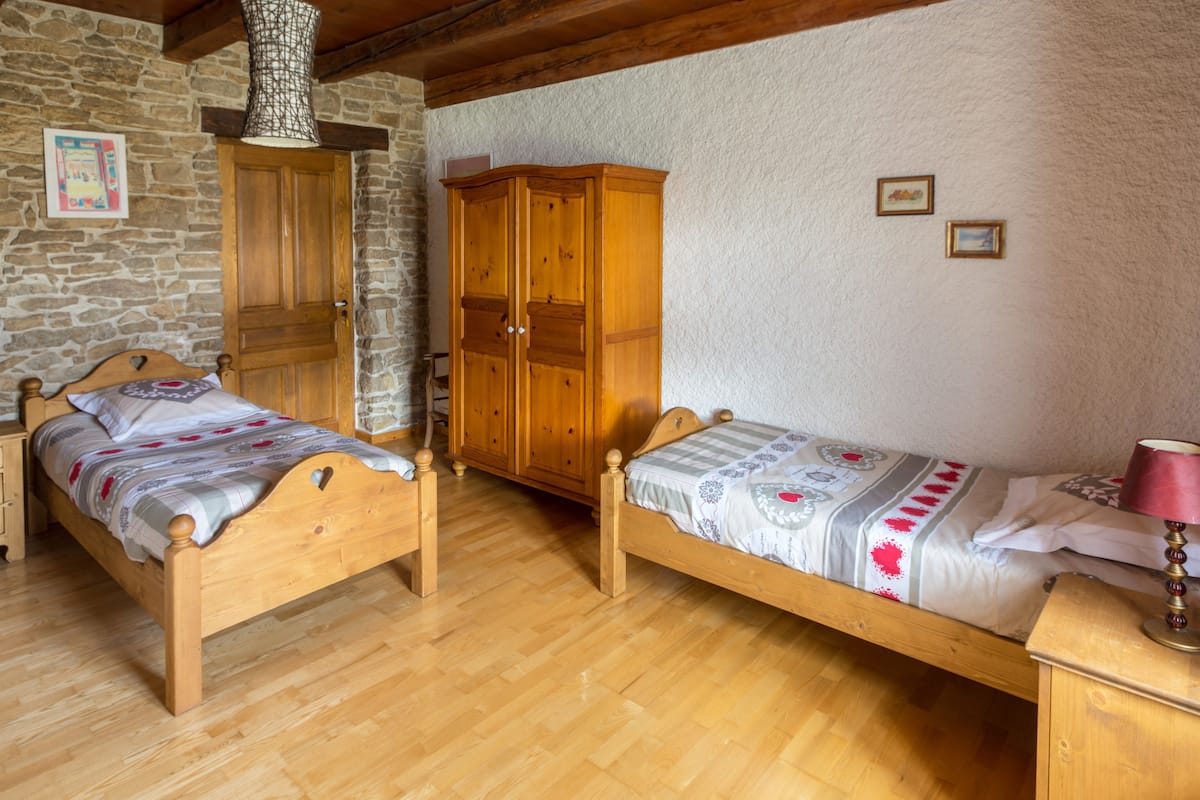 Une chambre avec deux lits en bois, une armoire et un mur en pierre.