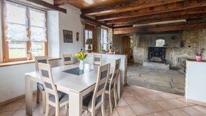 A rustic dining area with a wooden table and chairs, a vase of flowers, and a stone fireplace in the background. - La ferme Morin la Ronde Fontaine (Fournet-Blancheroche)