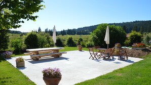 A picnic area with a concrete table and benches, surrounded by potted plants and a view of a forested hillside. - La ferme Morin la Ronde Fontaine (Fournet-Blancheroche)