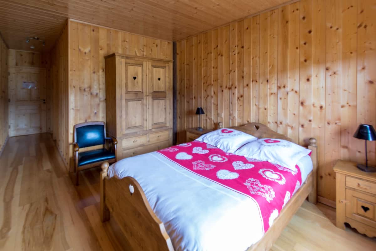 Une pièce aux murs lambrissés, contenant un lit, une chaise, une table de chevet et une armoire.