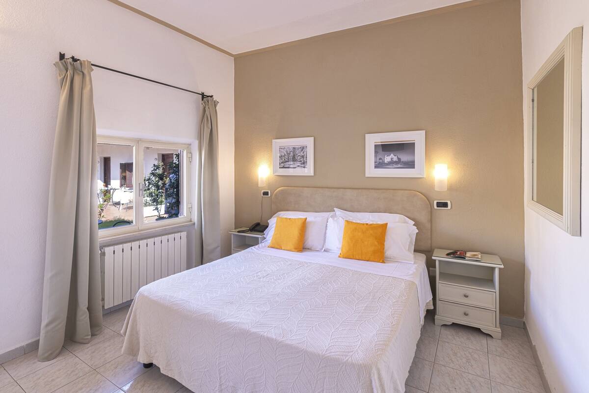 Een slaapkamer met een groot bed, twee nachtkastjes, een raam met gordijnen en twee wandlampen.