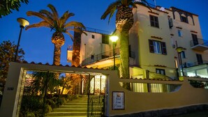 A hotel entrance with a wrought iron gate, palm trees, and a staircase leading to the entrance.