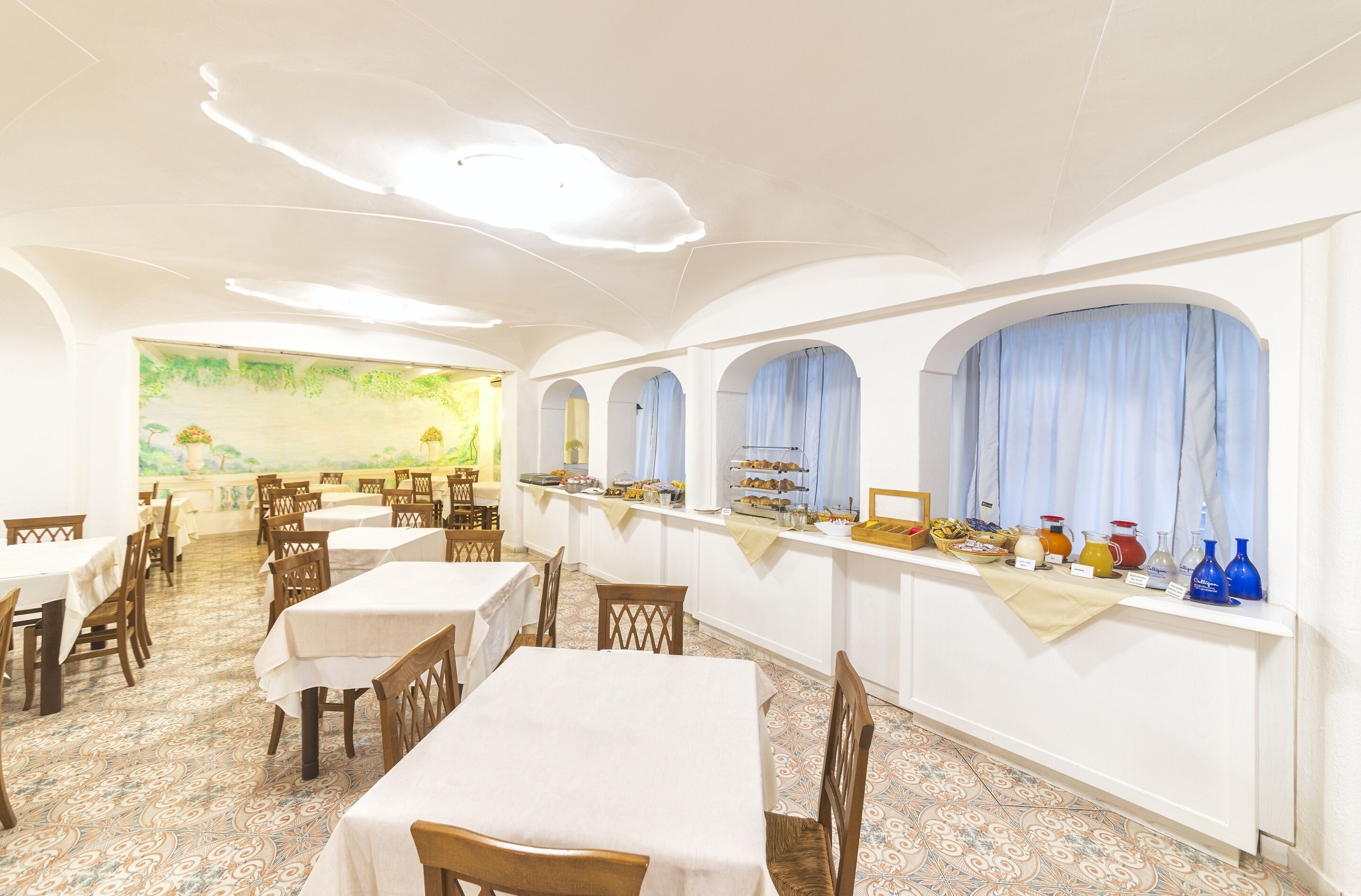 Un restaurante con mesas y sillas blancas, una barra de buffet con alimentos y un mural en la pared.