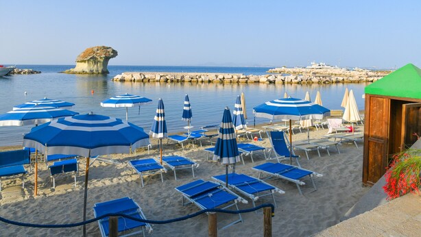 A beach with blue and white striped umbrellas, sun loungers, and a wooden structure.