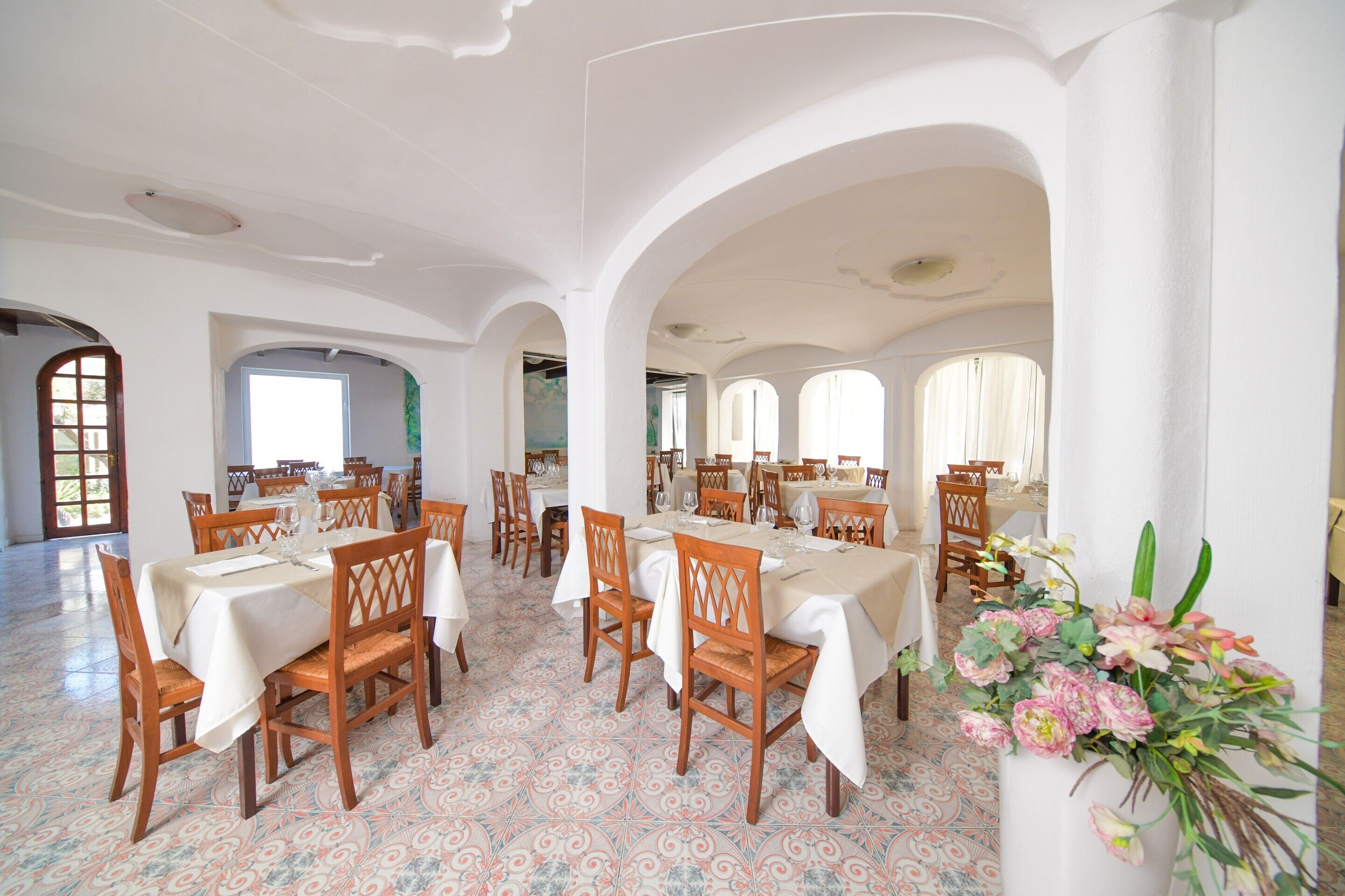 A dining area with multiple tables and chairs, white walls, and patterned floor tiles.