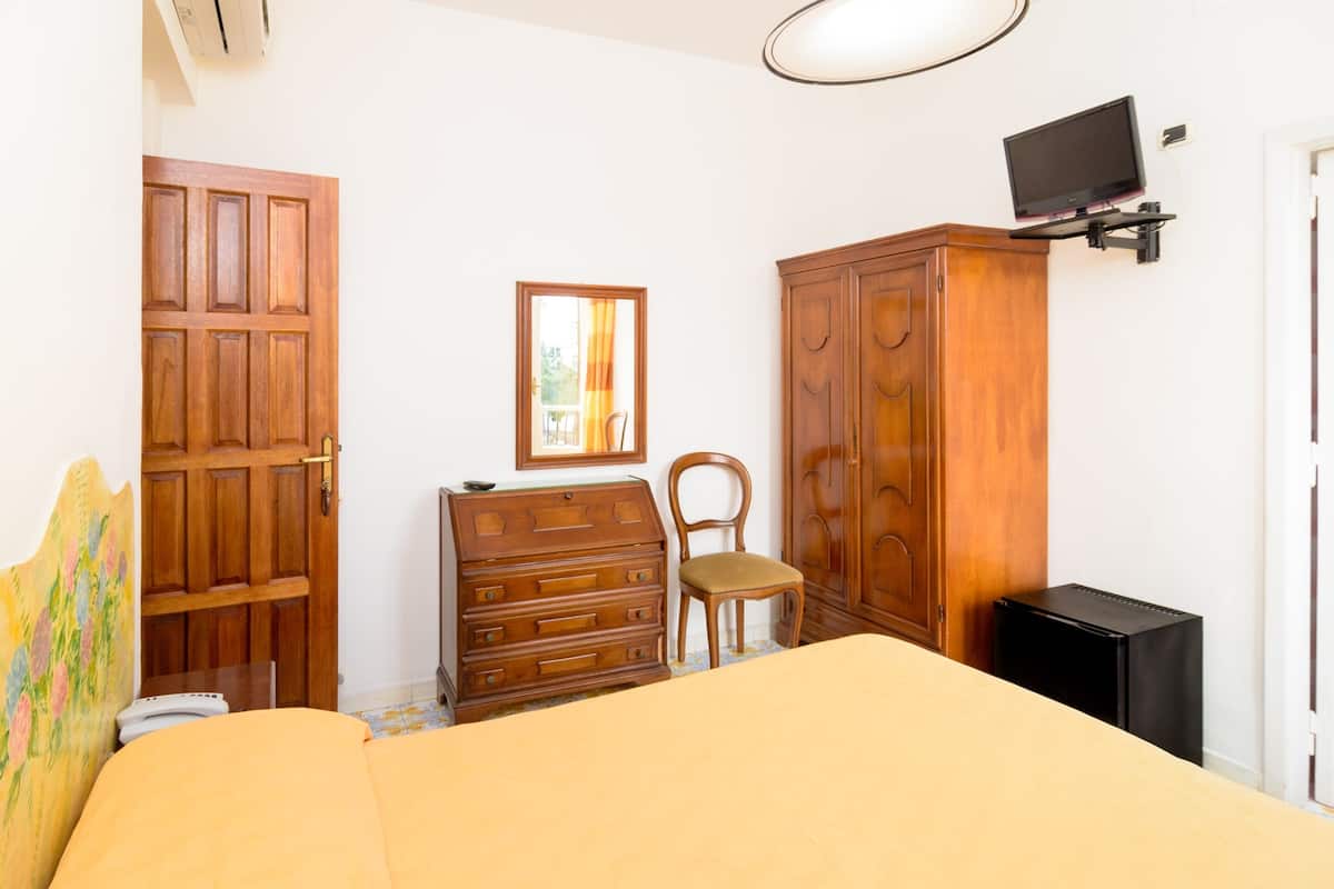 Een slaapkamer met een bed, een houten dressoir, een stoel en een aan de muur bevestigde televisie.