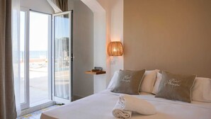 A hotel room with a bed, a window with curtains, a wall-mounted lamp, and a view of the beach.