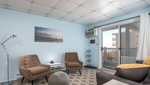 A room with a large window, two armchairs, a sofa, a floor lamp, and a patterned rug. - Oceanfront condos with 3 night minimum rentals and linens included! (Ocean City)