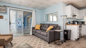 A modern living room with a grey sofa, a brown armchair, and a patterned rug. There is a kitchen area with white cabinets and a microwave. - Oceanfront condos with 3 night minimum rentals and linens included! (Ocean City)